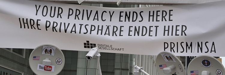 Am Checkpoint Charlie ein weißes Plakat mit schwarzer Schrift: "Your privacy ends here - Ihre Privatsphäre endet hier" und kleine Videokameras und Audioüberwachungsgeräte
