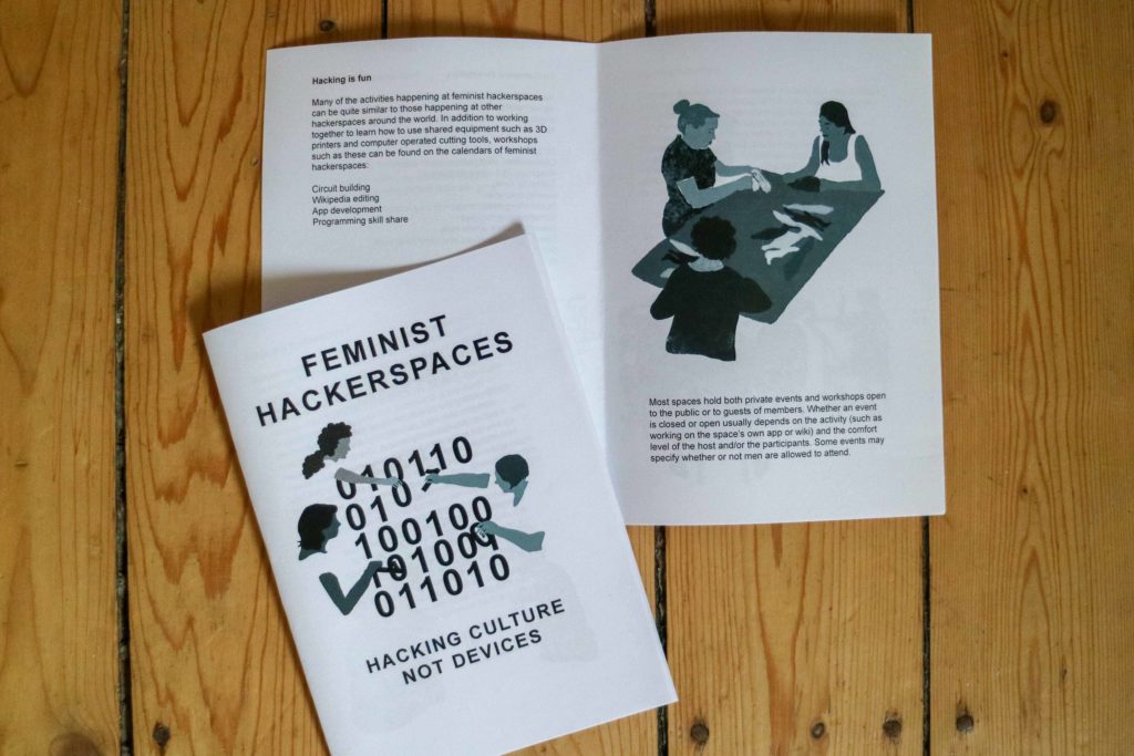 Eine Doppelseite Zine mit dem Titelbild von "Feminist Hackerspaces" auf Holzfußboden